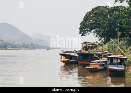 Bateaux traditionnels en bois laotien lent sur le fleuve du Mékong près de Luang Prabang, Laos, au coucher du soleil. Arrière-plan sur la montagne Banque D'Images