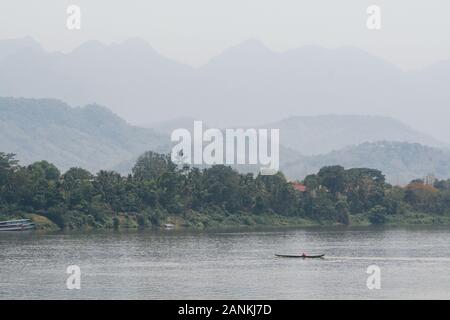 Bateaux traditionnels en bois laotien lent sur le fleuve du Mékong près de Luang Prabang, Laos, au coucher du soleil. Arrière-plan sur la montagne Banque D'Images