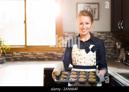 Une jeune femme présentant ses muffins aux copeaux de chocolat fraîchement cuits Banque D'Images