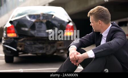 Contrarié homme assis sur route après accident de voiture de police d'attente, le manque d'expérience Banque D'Images