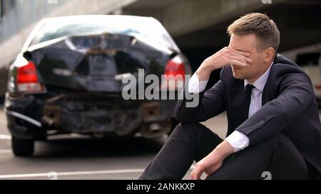 Homme désespéré assis sur l'asphalte est écrasé voiture contexte, accident de voiture Banque D'Images