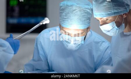 Chirurgien performing operation, sous-main tenant l'assurance-maladie, les outils médicaux Banque D'Images