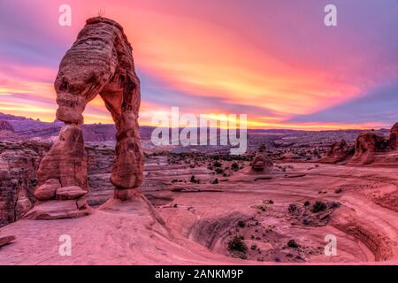 Delicate Arch perché sur le bord d'une crête circulaire contre un ciel de coucher du soleil à Arches National Park, Moab, Utah. Banque D'Images