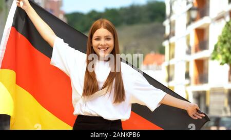 Adolescent aux cheveux rouges joyeuse en agitant le drapeau allemand et souriant à la caméra, le patriotisme Banque D'Images