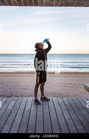 Jeune garçon sportif de boire une boisson isotonique sur la plage Banque D'Images