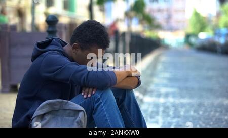 Bouleversé lonely boy multi-ethnique assis sur un trottoir, les conflits familiaux, la rébellion Banque D'Images