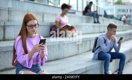Triste étudiante en tapant lunettes message smartphone campus séance escaliers Banque D'Images