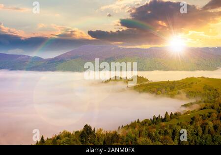 Paysages montagneux au coucher du soleil. vallée pleine de brouillard dans la lumière du soir. feuillage vert sur les arbres. merveilleuse nature paysage avec ressort en arc-en-ciel Banque D'Images