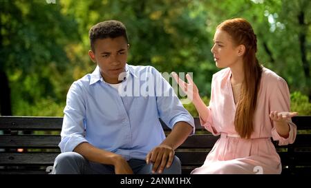 Couple multiethnique assis sur un banc de parc, la jalousie, l'incompréhension Banque D'Images