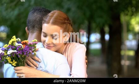 Afro Girl hugging boyfriend après avoir présenté, bouquet de fleurs, date Banque D'Images