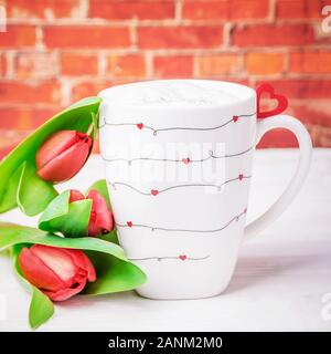 Happy Valentine's Day. Tasse de café latte. Tasse avec de petits cœurs rouges et des tulipes sur le fond de la brique Banque D'Images