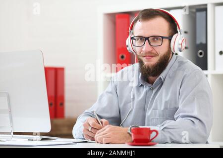 Un homme en casque d'écoute de la musique et apprend en ligne. Prend des notes sur un ordinateur portable et s'intéresse à l'appareil photo Banque D'Images