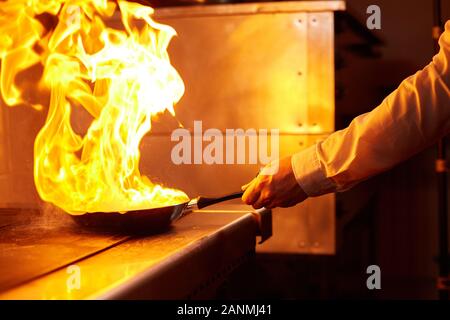 Flambe. Feu dans la poêle à frire. Chef professionnel dans une cuisine commerciale. Faites frire des aliments dans une poêle moulante sur la table de cuisson dans la cuisine extérieure Banque D'Images