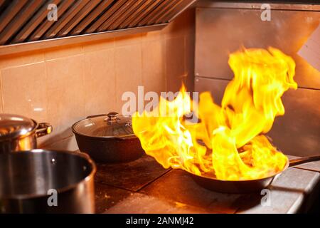 Flambe. Feu dans la poêle à frire. Chef professionnel dans une cuisine commerciale. Faites frire des aliments dans une poêle moulante sur la table de cuisson dans la cuisine extérieure Banque D'Images