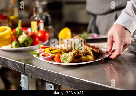 Le chef prépare dans le restaurant. Carré d'agneau grillé avec frites et légumes frais Banque D'Images