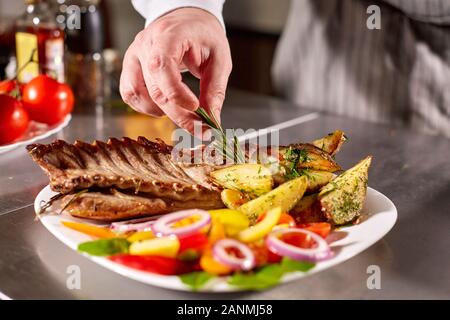 Le chef prépare dans le restaurant. Carré d'agneau grillé avec frites et légumes frais Banque D'Images