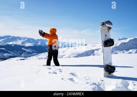 Homme avec photographie Téléphone sur Paysage de neige près de Snowboard et de sports d'hiver Accessoires Banque D'Images