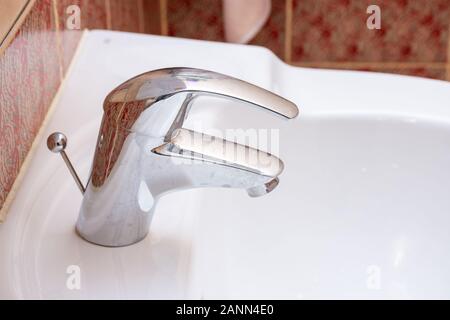 Robinet de salle de bain résidentiel brillant argent ou appuyez sur un évier en céramique blanche. La plomberie, bricolage, d'entretien ou de concepts. Banque D'Images