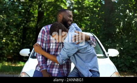 Père aimant présentant la clé de l'automobile, son fils adolescent heureux parents hugging Banque D'Images