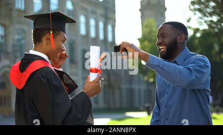 Smiling dad en vidéo smartphone de professionnels diplômés fils avec diplôme, d'un événement Banque D'Images