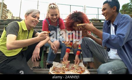 Les jeunes gens heureux de manger des pizzas à l'extérieur, les amis de détente en plein air Banque D'Images