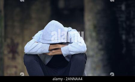 Triste afro-american teenager dans hood assis rue, pensant de problèmes Banque D'Images