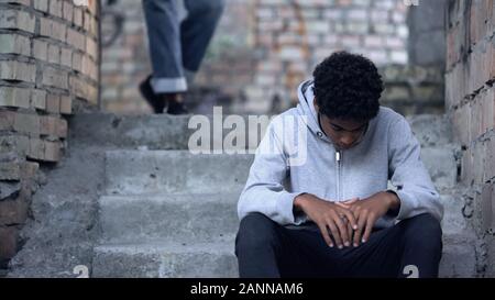 Triste adolescent noir assis sur des escaliers dans gateway, problème de l'intimidation à l'école Banque D'Images