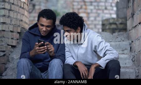Les adolescents assis dans la maison abandonnée de regarder la vidéo passionnante sur le smartphone. Banque D'Images