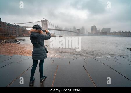 Femme de tourisme avec des vêtements chauds prenant une photo du pont de Brooklyn Banque D'Images