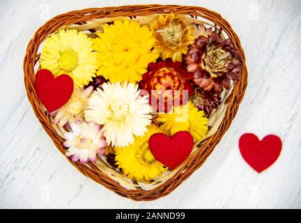 En forme de coeur un panier plein de fleurs séchées et quelques coeurs rouges Banque D'Images