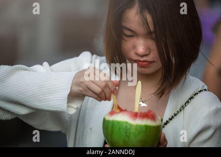 Feng Huang, Chine - Août 2019 : Chinese girl eating pièces de coupe de délicieux et ripe melon dans la rue dans la vieille ville en Feng Huang, Huna Banque D'Images