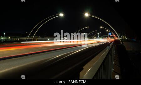 Phare de voiture rouge et blanche de nuit sur des sentiers de pont, entouré de panneaux lampadaires ; fournir des lignes diagonales profondeur et vitesse Banque D'Images