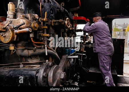 Focalisation sélective sur les éléments ou les pièces du moteur à vapeur dans la cabine du train à vapeur avec un ingénieur ou un conducteur de train non reconnaissable travaillant sur les manivelles, en Irlande Banque D'Images