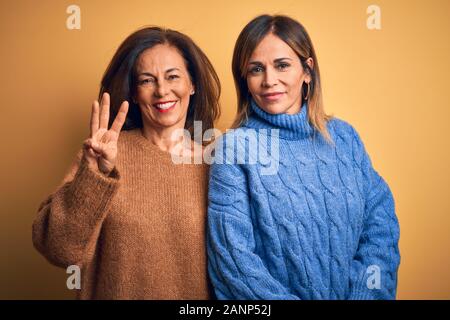 L'âge moyen beau couple de soeurs portant chandail occasionnels sur fond jaune isolés montrant et pointant vers le haut avec les doigts tout en numéro trois Banque D'Images