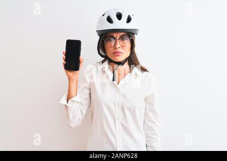 Young Woman holding smartphone casque de vélo sur fond blanc isolé avec une expression confiante face à la pensée intelligente grave Banque D'Images