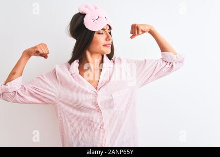 Belle Jeune femme portant un masque de sommeil et plus de pyjama fond blanc isolés montrant les muscles des bras fier sourire. Concept de remise en forme. Banque D'Images