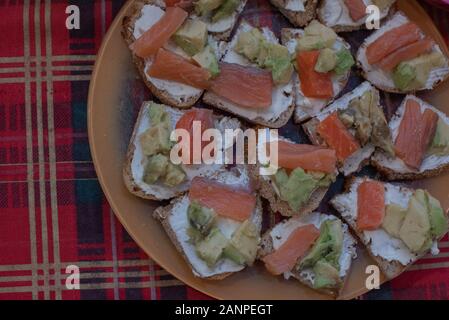Toasts à l'avocat et saumon fumé. Sandwiches au saumon et d'avocat. Sandwiches au saumon et d'avocat et de fromage sur une assiette sur la table. Banque D'Images