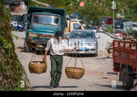 Pingan, Chine - Août 2019 : vieux Chinois transportant une charge lourde de fruits en vente jusqu'aux pentes escarpées en chemin, Pingan Longji terrasses de riz, l'Hepi Banque D'Images