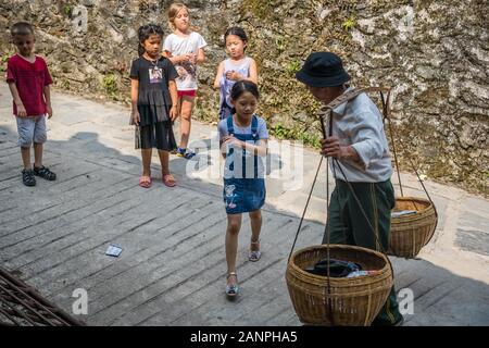 Pingan, Chine - Août 2019 : Curieux village enfants vieille chinois transportant une charge lourde de fruits à vendre à Pingan Longji, Rice Terr Banque D'Images