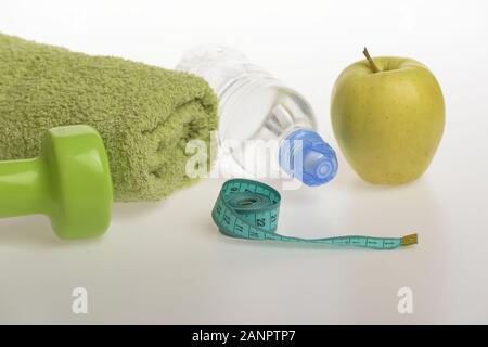 Sport et régime sain de l'équipement. Régime alimentaire et régime sport concept. Barbell en plastique près de green apple. Haltère en vert, une bouteille d'eau, mesurer la bande, serviette et fruits sur fond gris Banque D'Images