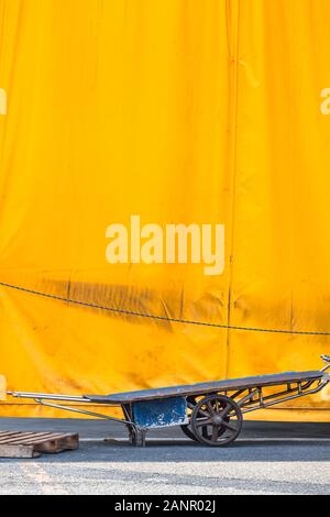 Bâche jaune background avec de vieux matériel de transport trolley et sur palettes de cour asphaltée (copie espace) Banque D'Images