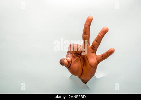 la personne noire a la main à travers un trou dans un carton faisant signe ok, montrant trois doigts Banque D'Images