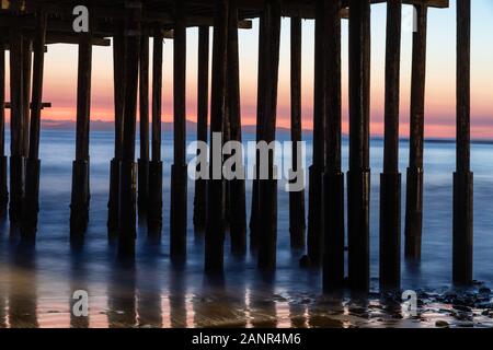 Près de piliers, Jetée de Ventura, Ventura, Californie. Retrait de l'eau à marée basse, le sable et les roches visibles. Ciel de couleur en arrière-plan. Banque D'Images