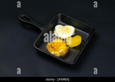 Un petit poêlon noir avec des oeufs de cailles en forme de cœur, à côté de celui-ci sont bell pepper sur le fond noir. Top vues Banque D'Images