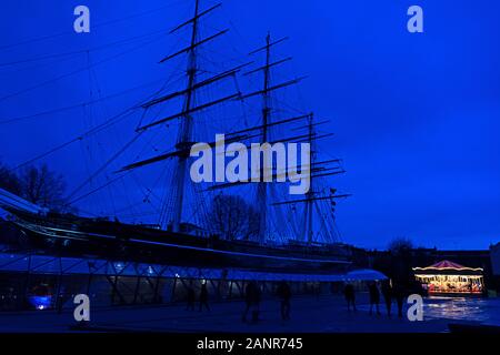 Lumières d'un carrousel brillants dans le crépuscule d'hiver sont éclipsées par la silhouette de l'nearcy Cutty Sark, Greenwich, Angleterre. Banque D'Images