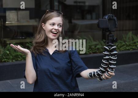 Jeune fille caucasienne souriante femme faisant un blog vidéo (vlog) avec caméra à l'extérieur dans la rue Banque D'Images