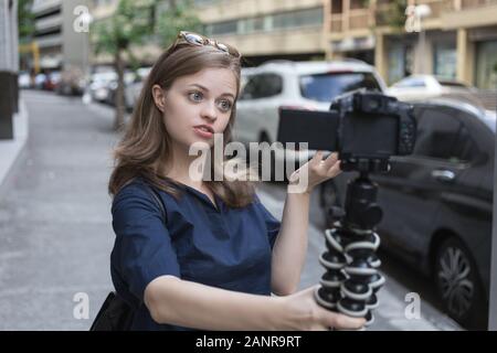 Jeune fille caucasienne souriante femme faisant un blog vidéo (vlog) avec caméra à l'extérieur dans la rue Banque D'Images