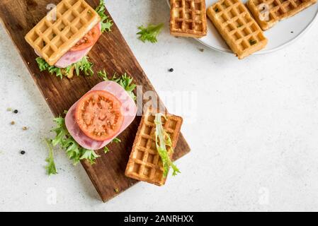 Gaufres salées au jambon et tomate sandwich pour le petit-déjeuner céto. Chaffle (fromage et d'oeufs gaufre) sandwich sur white, vue du dessus, copiez l'espace. Banque D'Images