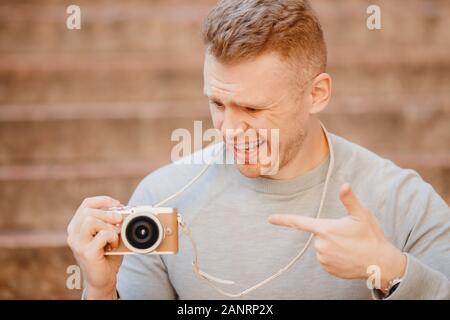 Photographe voyageur mâle avec petit appareil photo en mains, surpris de compacité et légèreté de l'appareil Banque D'Images