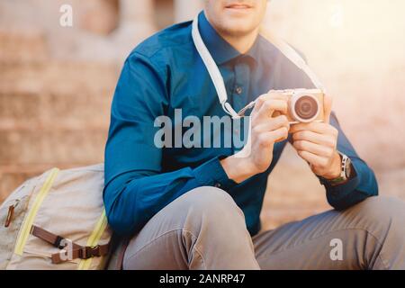 Photographe voyageur mâle avec petit appareil photo en mains, chemise bleue et son sac à dos Banque D'Images